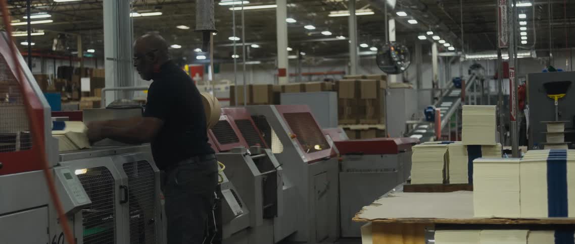 Worker places stack on machine sitting over conveyor belt in factory