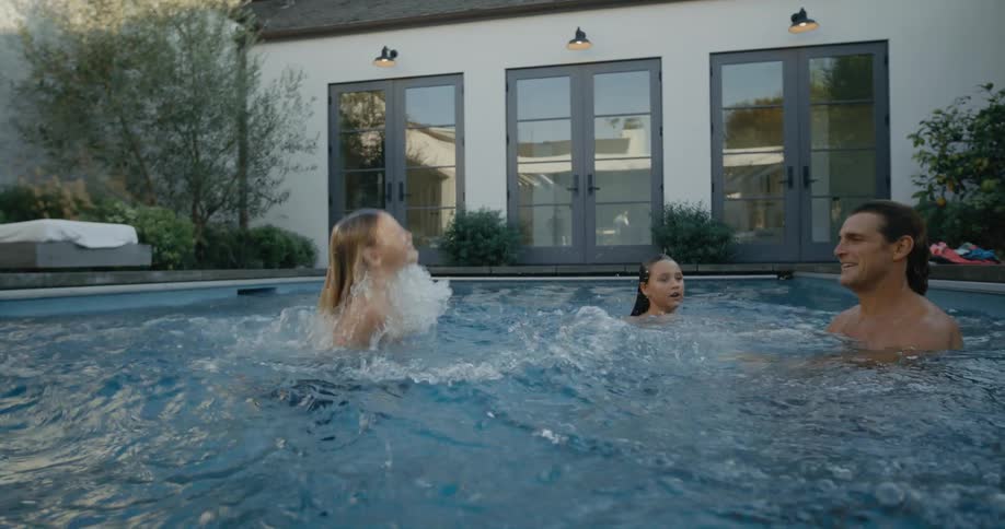 As family plays in the pool father throws his son backward into the water
