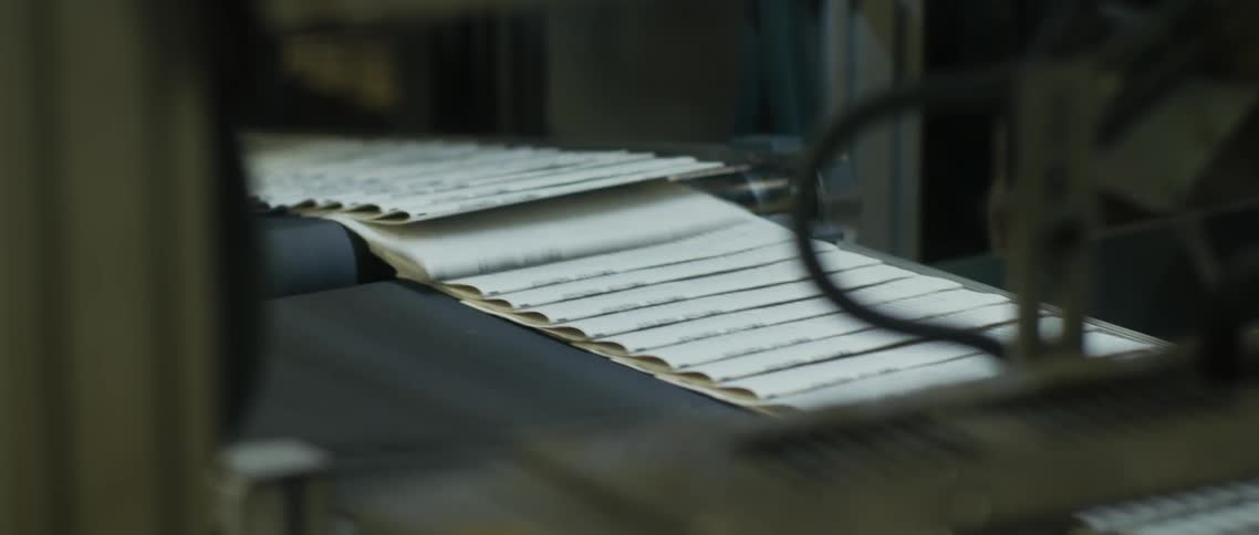 A man removes paper as it comes down a conveyor belt in a factory