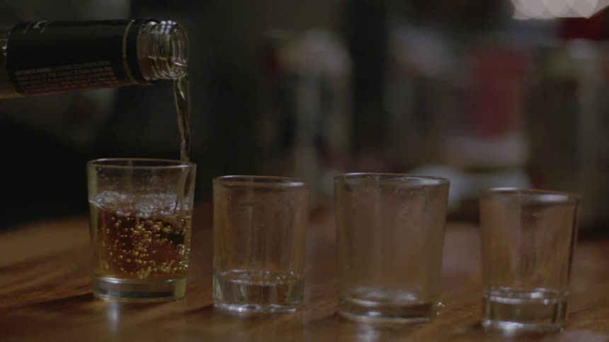 Liquor being poured into several shot glasses