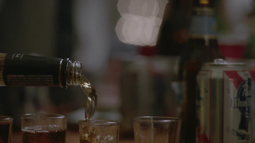 Alcohol is poured from a bottled into shot glasses