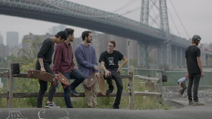 A row of people sit against a fence as others skateboard