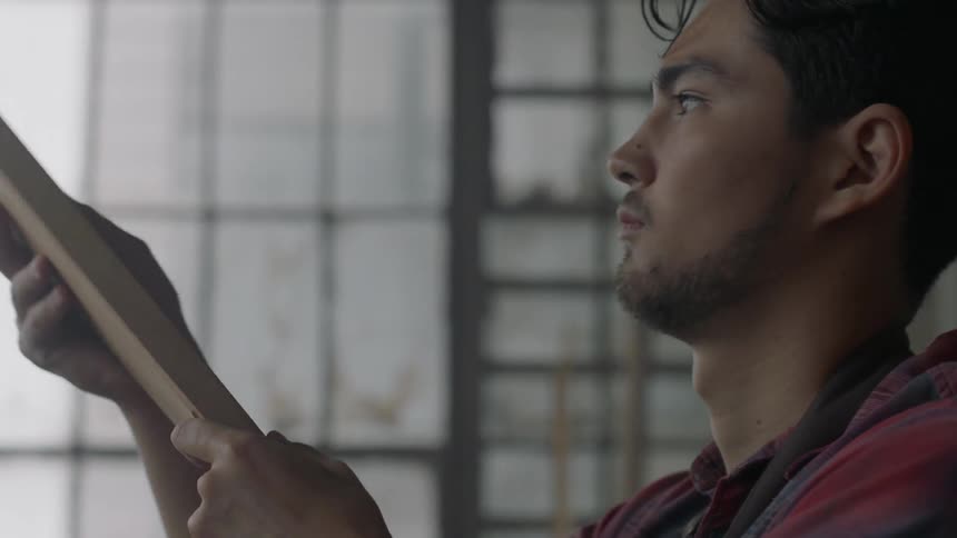 A man examines a piece of wood in building during the day