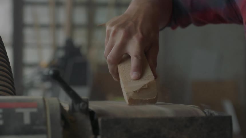 A man sands a block of wood on a sanding belt