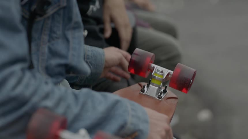 Someone holding a skateboard on their lap spins the skateboard's wheels