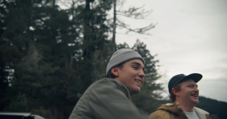 Two men laugh and throw rocks while standing on a river bank