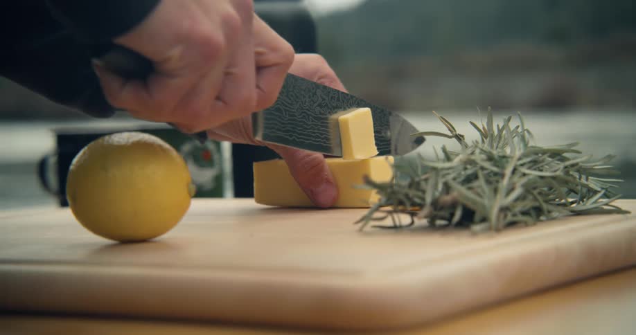 A man cuts pats of butter on a cutting board set up near the river