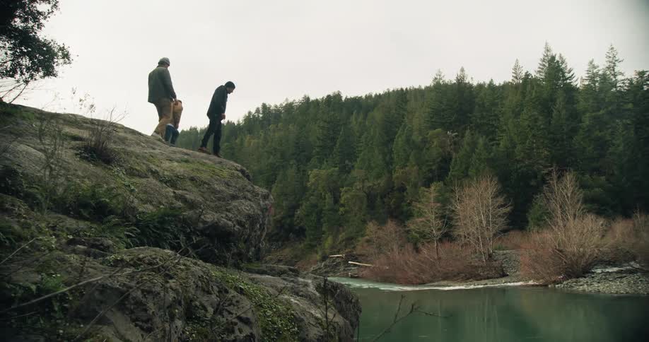 Three men walking towards the cliff of a big rock next to the river at a forest area