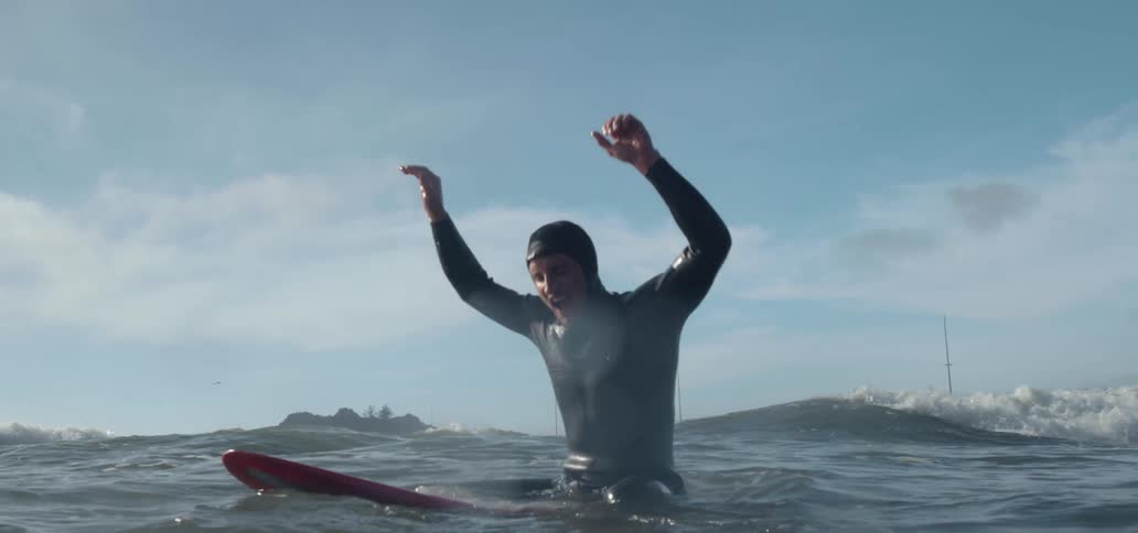 Man wearing a wetsuit sitting in the surfboard at the ocean at a sunny day and cheering