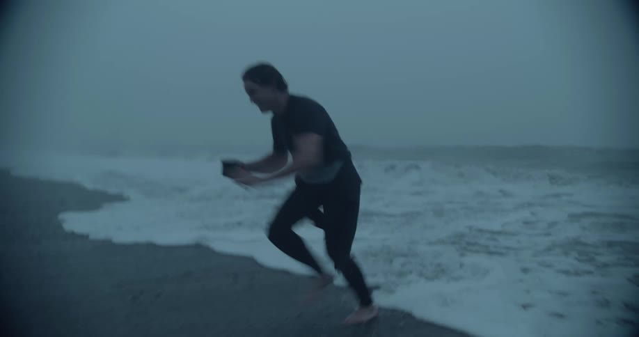 Man running towards the sea and then running back while holding a cup at the beach
