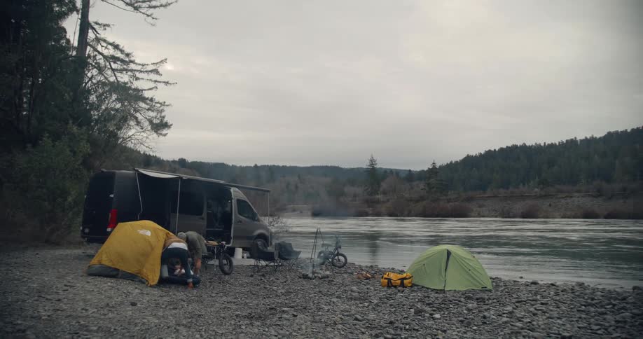 Two people setting up a tent on a river bank