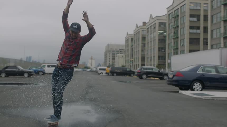 Person skateboarding through a small puddle on a city street