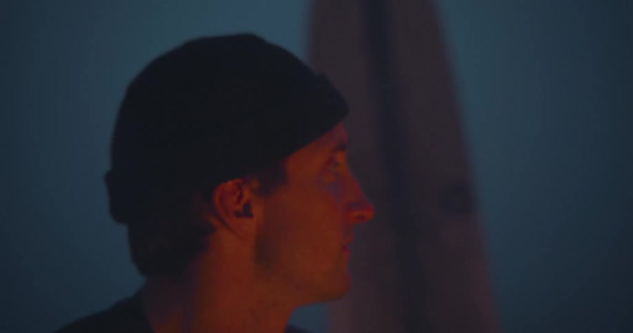 Man wearing a winter beanie sitting next to a campfire with his face lightened by the fire