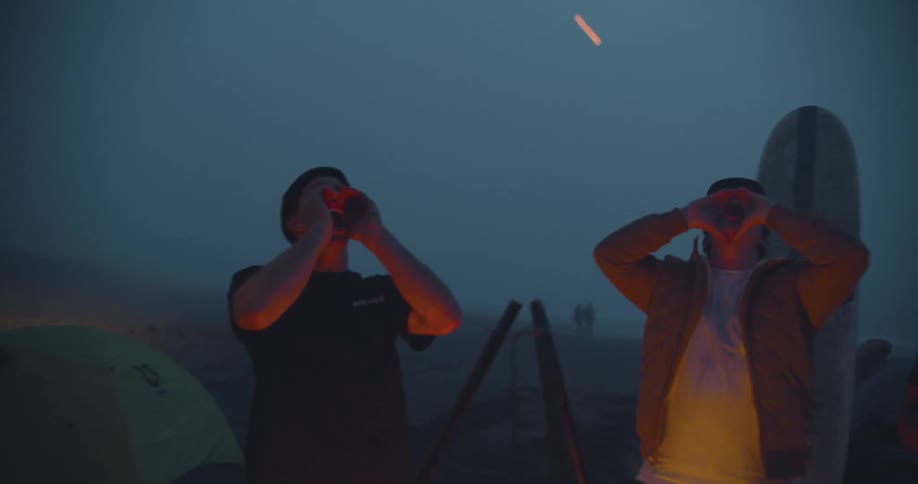 Three friends standing around a campfire at the beach and screaming as loud as they can