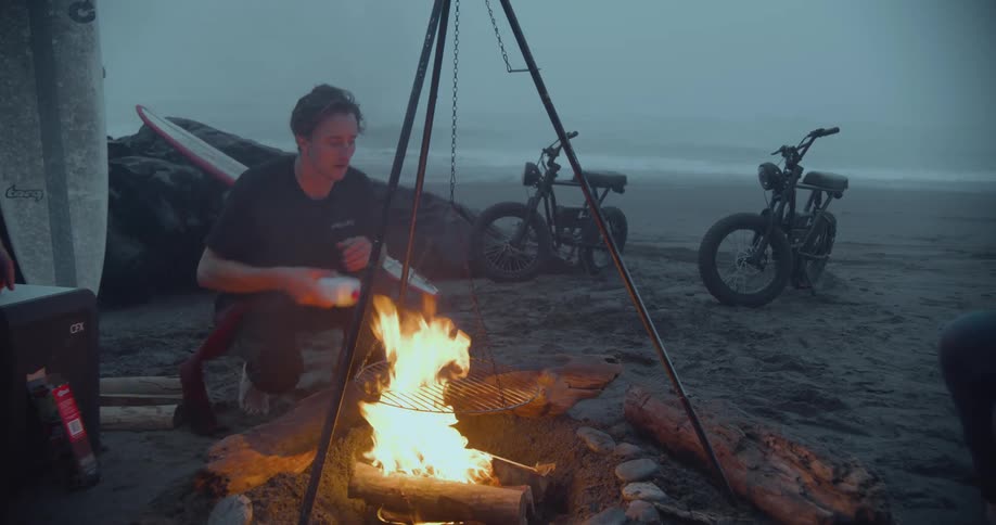 A man adds copious amounts of lighter fluid to a campfire on the beach