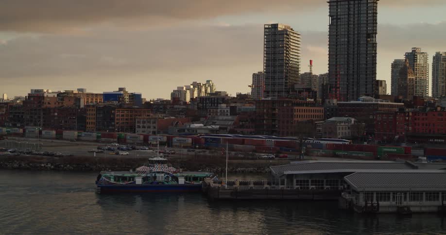 A sea bus pulls into a waterfront station in a metropolis at sunset