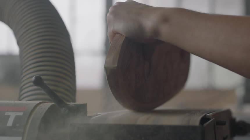 A man sands the edges of a plank of wood