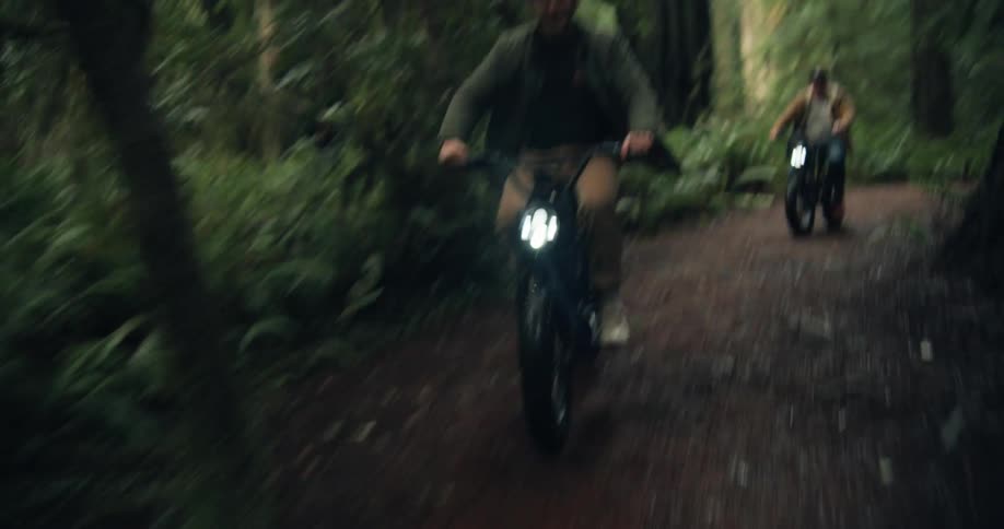 Two men are riding their bikes on a trail in a forest