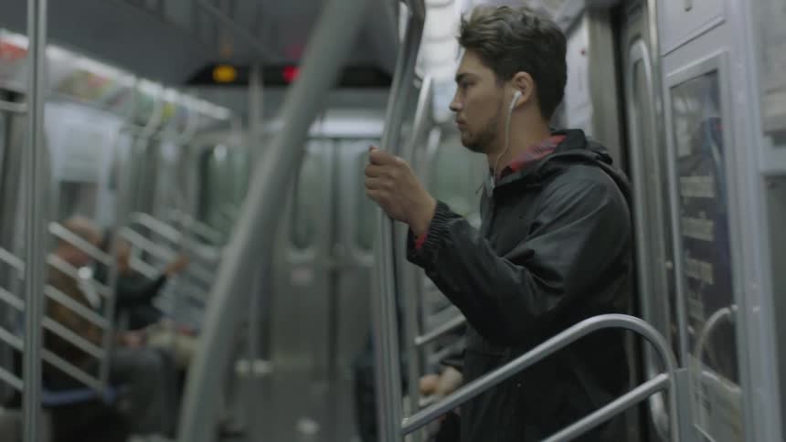 Man wearing earbuds standing in a subway train