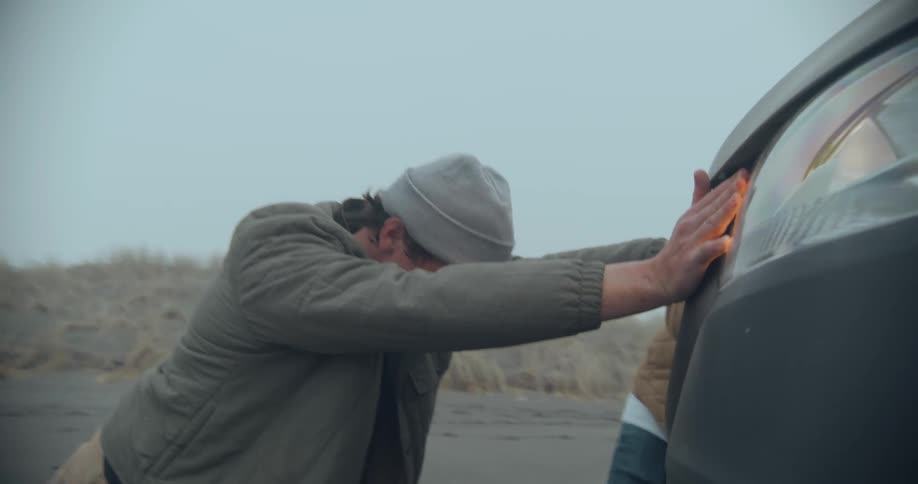 Two men trying really hard to push a grey car