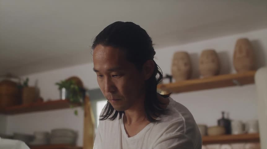 A man cooks with his baby sitting on the counter in a chefs hat