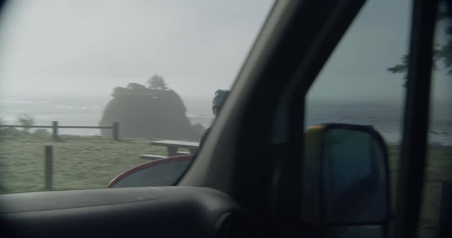 A vehicle stops to let in a man carrying a surfboard on the coast during the day