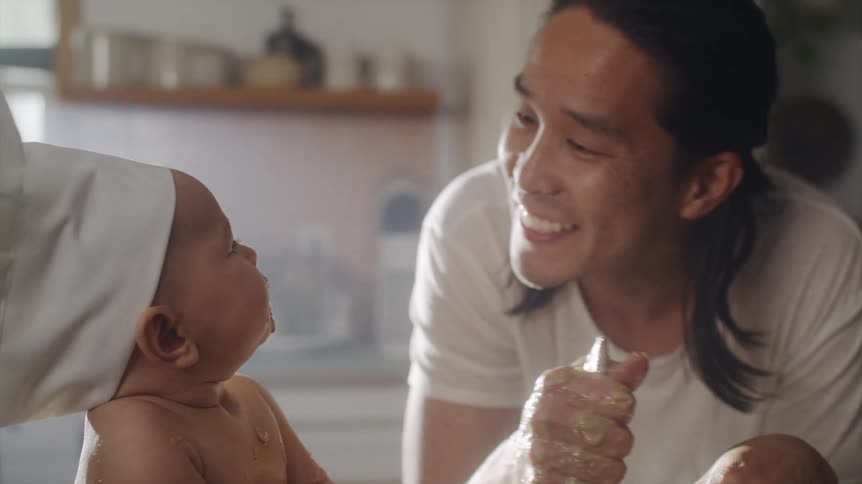Father cooking at the kitchen counter while talking and kissing his baby that is sitting next to him