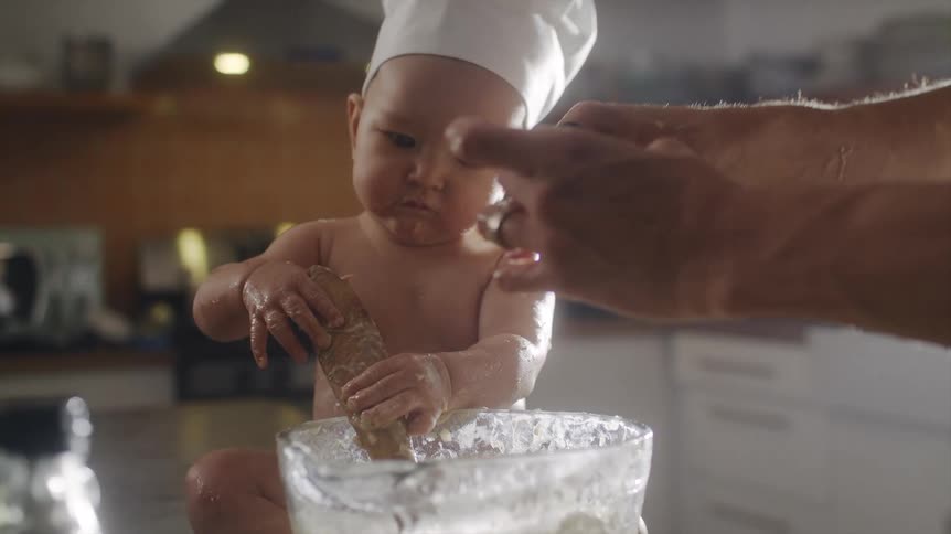 A man has his baby help mix batter while cooking at home