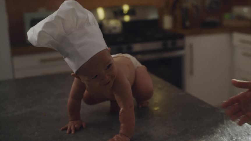 Baby wearing a chefs hat at the kitchen counter smiling and laughing with his father
