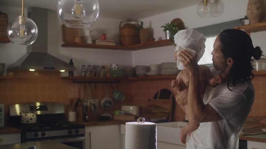 A man cooking in a kitchen wipes his babys face and kisses him