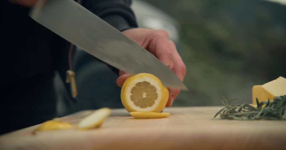 Man standing outdoors cutting an orange in a cutting board with a chefs knife