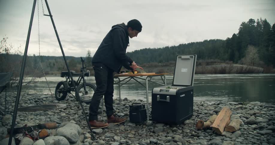 Man cutting some food at a mini table in a camp near a river