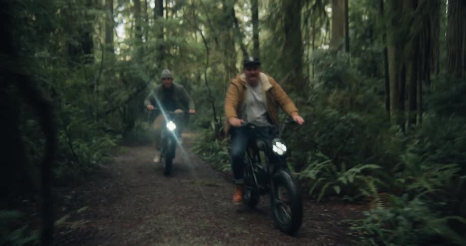 Two men are riding their bikes on a trail in a forest