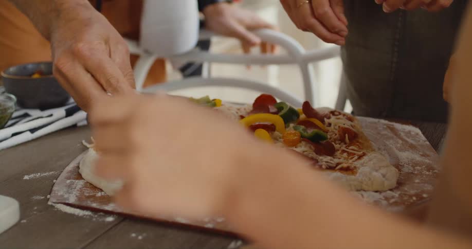 Three people putting ingredients on top of a pizza dough on the table