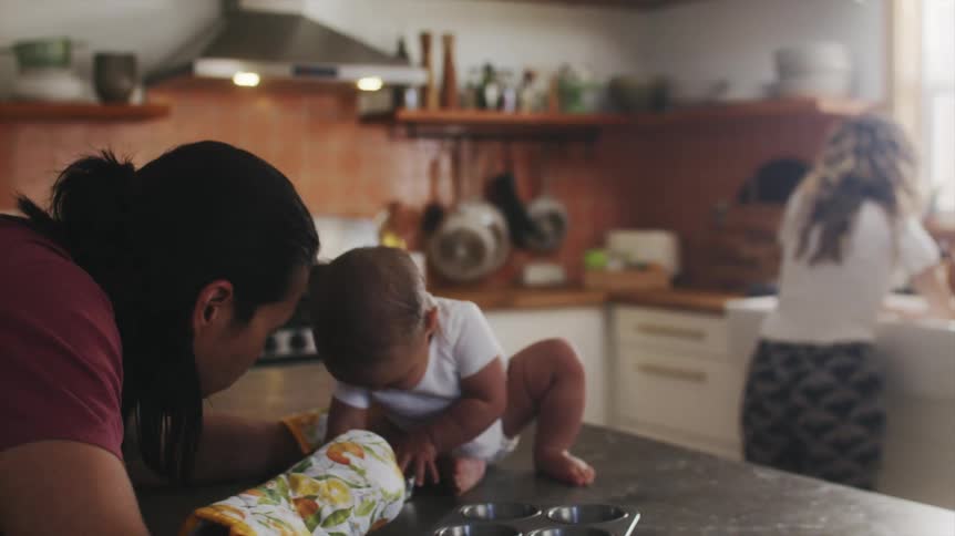 Father give baby muffin as mother works at sink