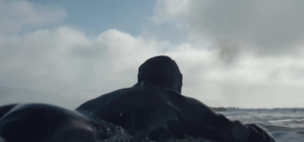 Surfer getting on surfboard in the ocean then paddling out