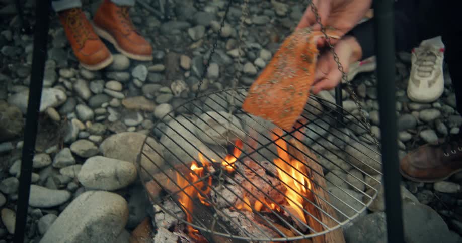 Man taking a piece of salmon and putting it to grill on a campfire in an outdoor camping
