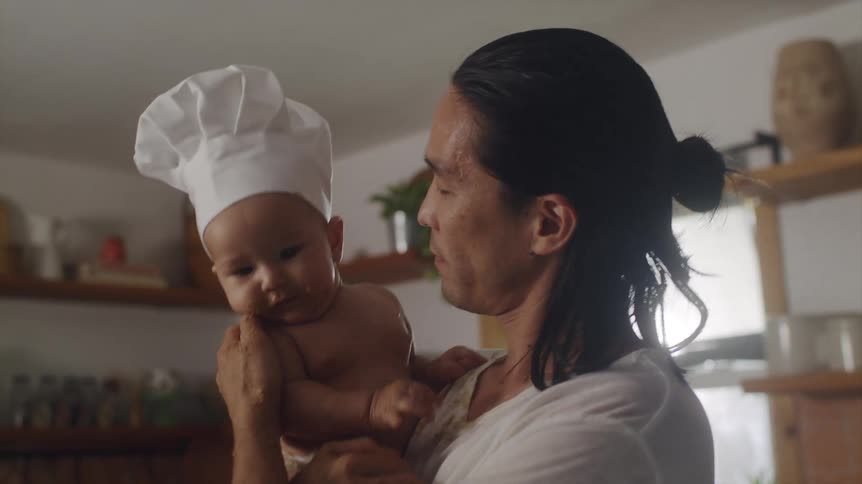 Father picking up baby wearing chef hat from counter then kissing and playing with him