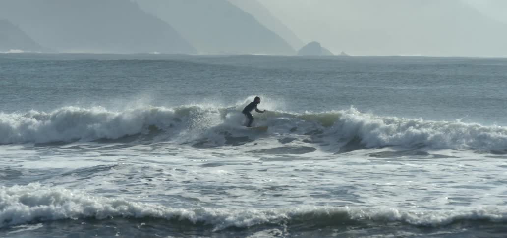 A surfer is riding a wave and his surfboard flies into the air as he goes underwater
