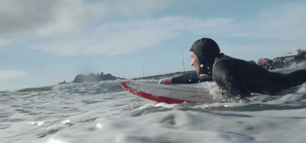 Man wearing a male wetsuit swimming on a surfboard and getting ready to surf a wave