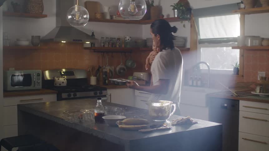 Man holds an infant as he puts a muffin pan into the oven