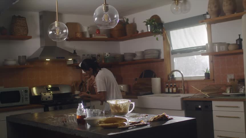 Father with long hair white shirt and apron carries baby son with chef hat and diaper putting muffin tin in oven