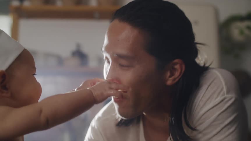 A man allows a baby in a chef hat to play with his face