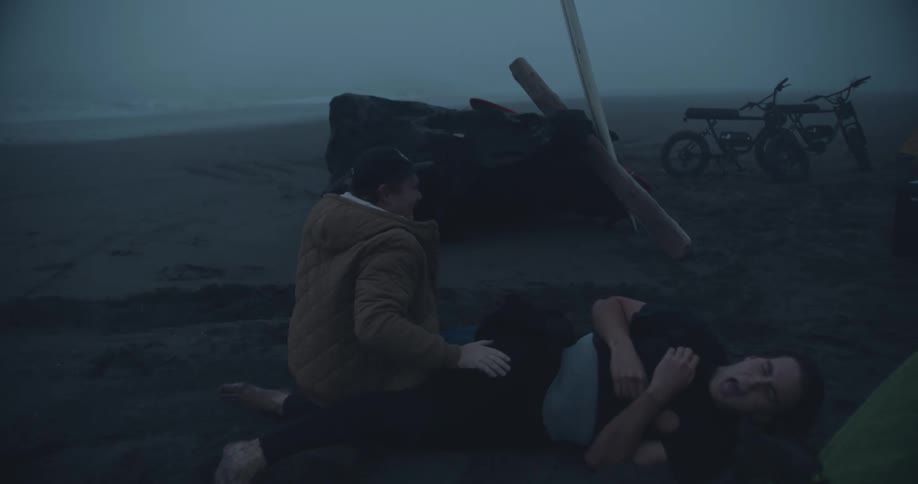 Two men wrestle around on the beach