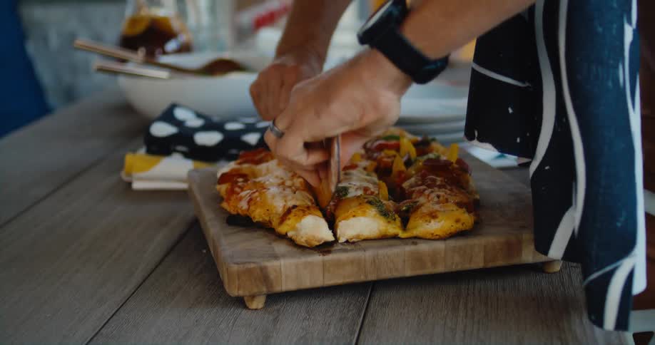 Man slicing a deep dish homemade pizza with a rocker pizza knife