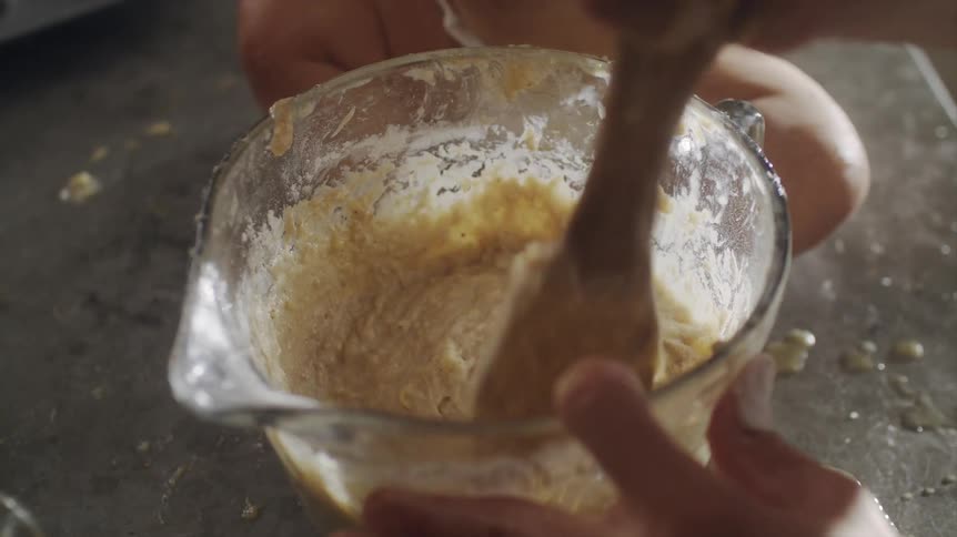 Man preparing food in the kitchen mixing a cream in a glass bowl while a baby is sitting next to it
