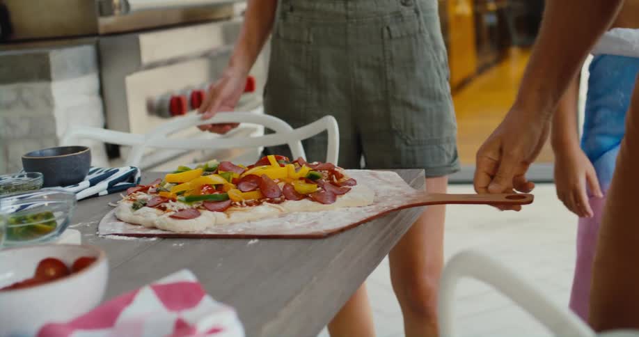 A group of friends prepare a pizza in the kitchen
