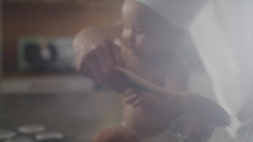 A man uses his fingers and a spoon to mix muffin batter while his baby watches