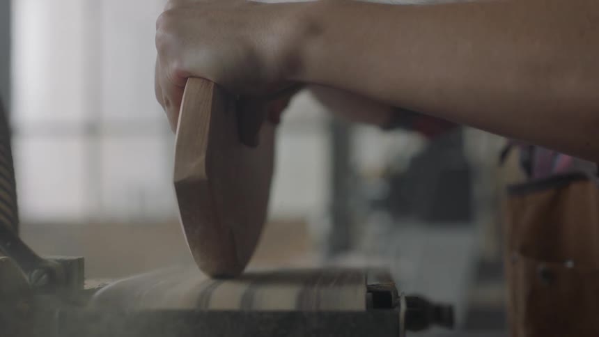 A man sands the edge of a board of wood on a sander