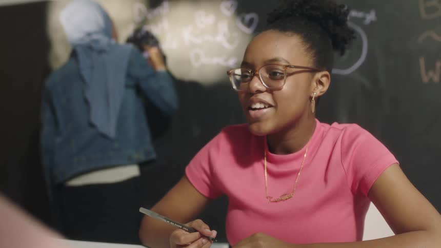 A young woman speaks while writing with a pen in a classroom during the day